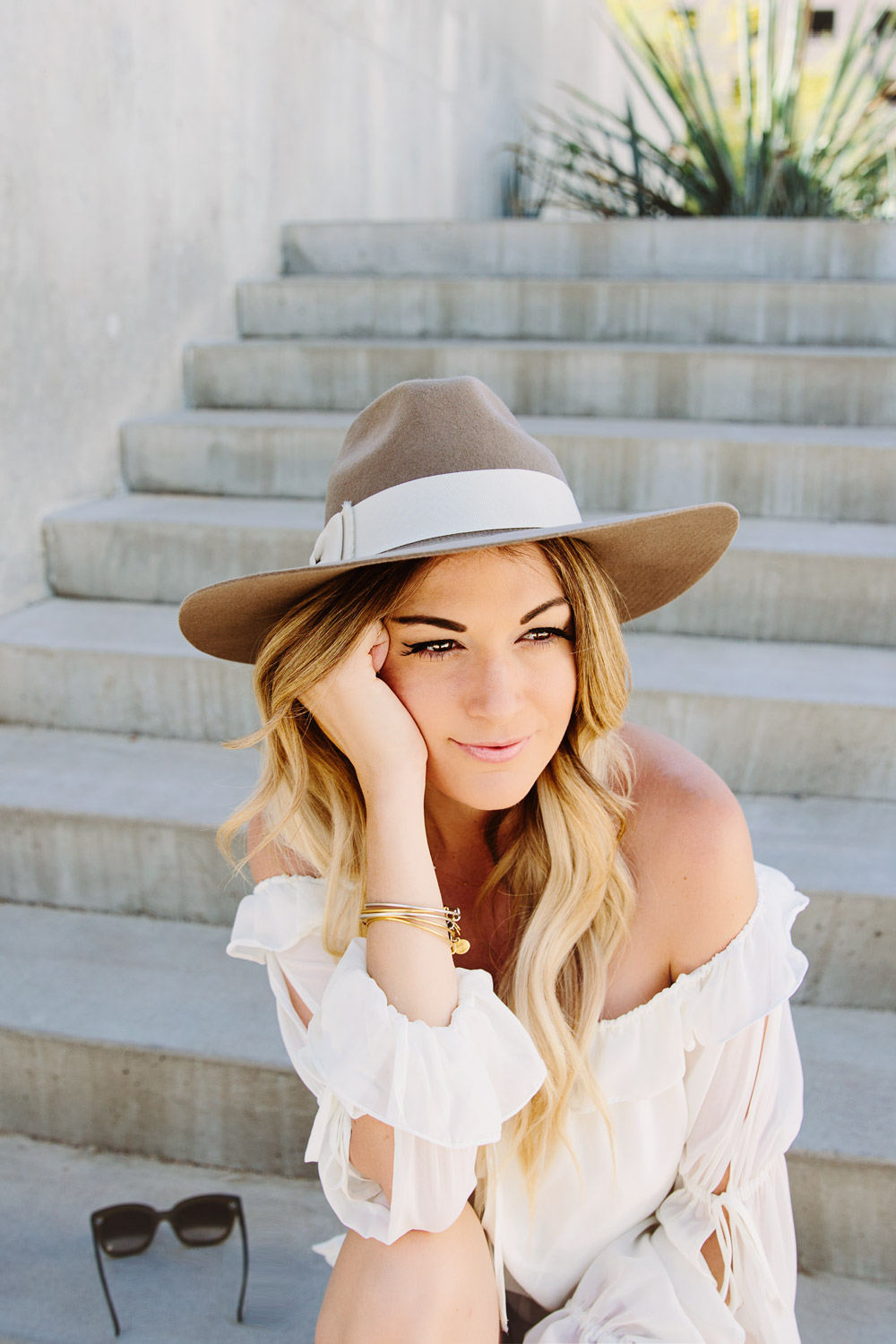 Dash of Darling wears a white off shoulder ruffled hem romper with a wide brim hat for the perfect summer outfit.
