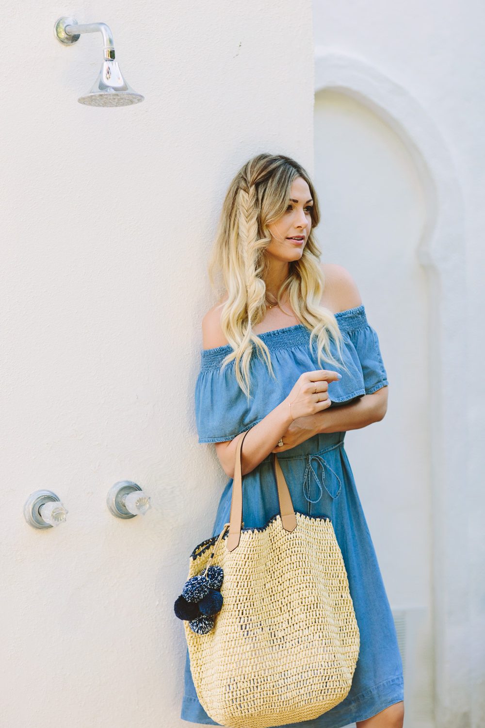Caitlin Lindquist of Dash of Darling styles a chambray off shoulder dress from LOFT with a pom pom straw tote and wedge sandals for a summer look while in Palm Springs.