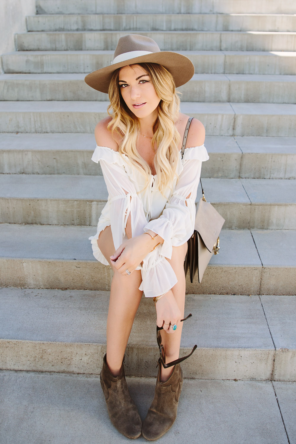 Dash of Darling styles a white off shoulder ruffled hem romper with a wide brim hat, Isabel Marant booties and the Chloe Faye leather bag for the perfect summer look.