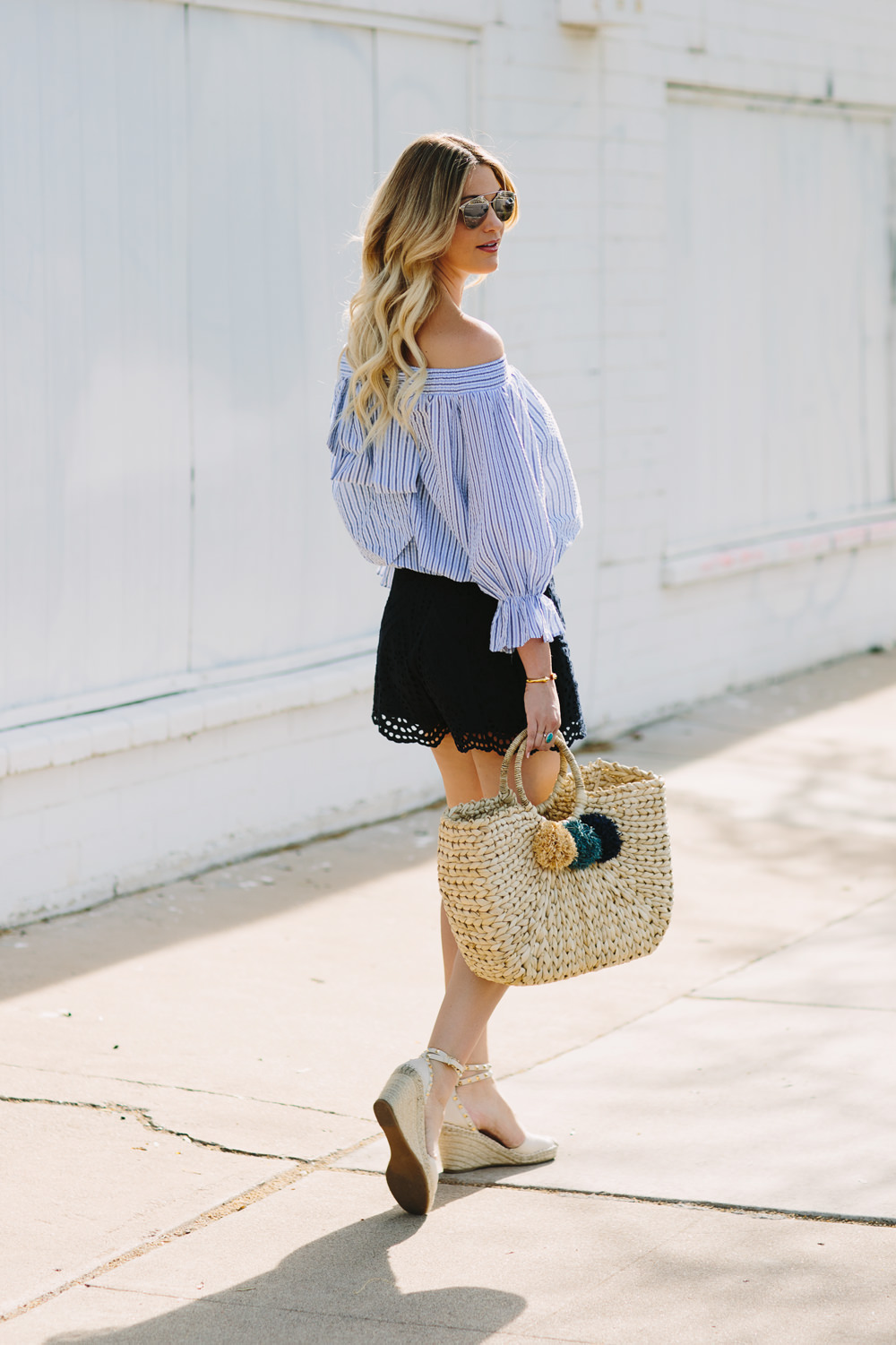 Dash of Darling styles a pastel blue Chicwish stripe off shoulder bow top with Zimmermann lace shorts and a woven beach tote for a summer outfit.