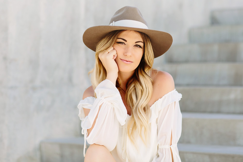 Dash of Darling wears a white off shoulder ruffled hem romper with a wide brim hat by Hat Attack  for a bohemian summer look.
