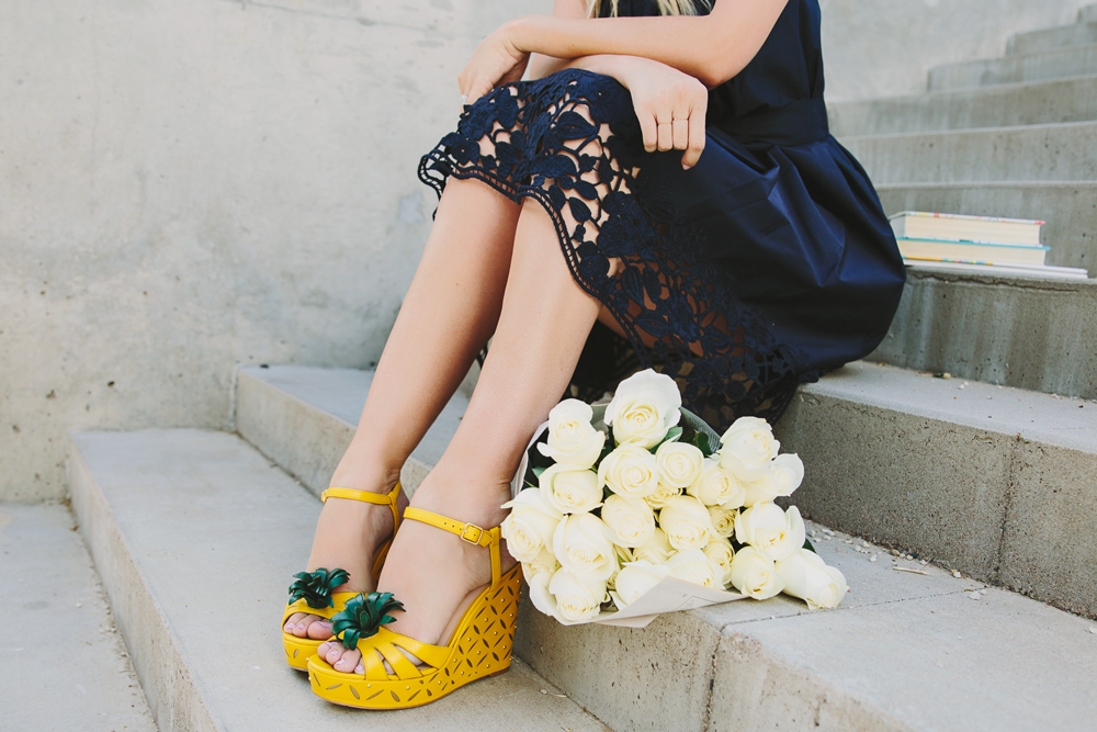 Dash of Darling styles a kate spade navy embroidered dress with yellow pineapple wedges and a white cross body bag.