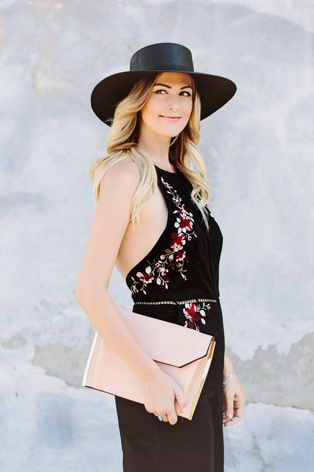 Caitlin Lindquist of Dash of Darling wears a Zimmermann floral embroidered black jumpsuit with a Janessa Leone straw hat  for a summer outfit perfect for a wedding.