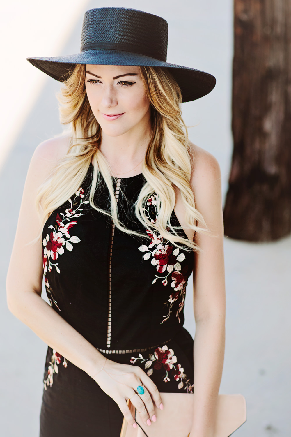 Caitlin Lindquist of Dash of Darling wears a Zimmermann floral embroidered black jumpsuit with a Janessa Leone straw hat for a summer outfit perfect for a wedding.