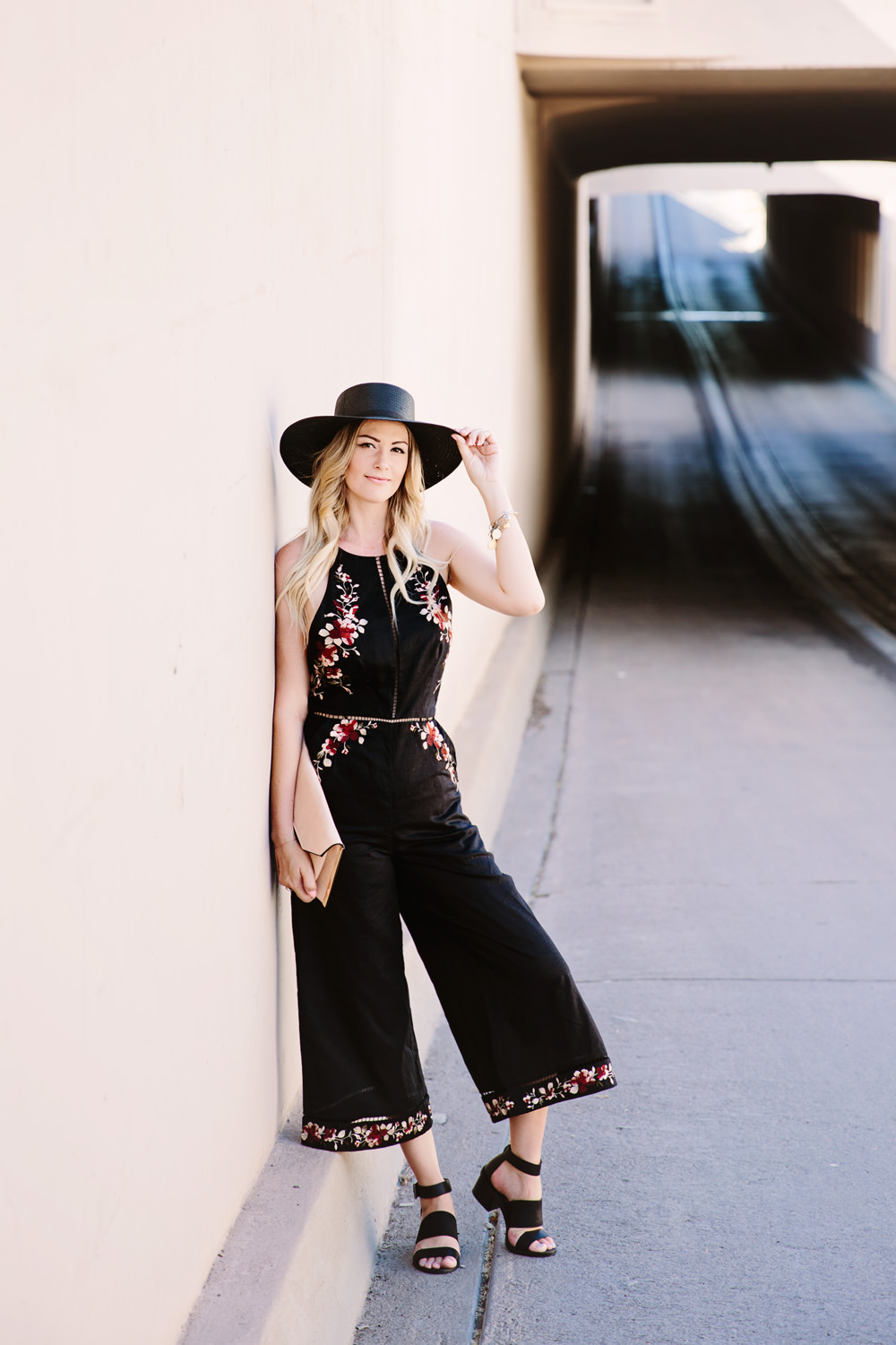 Caitlin Lindquist of Dash of Darling wears a Zimmermann floral embroidered black jumpsuit with a Janessa Leone straw hat for a summer outfit perfect for a wedding.