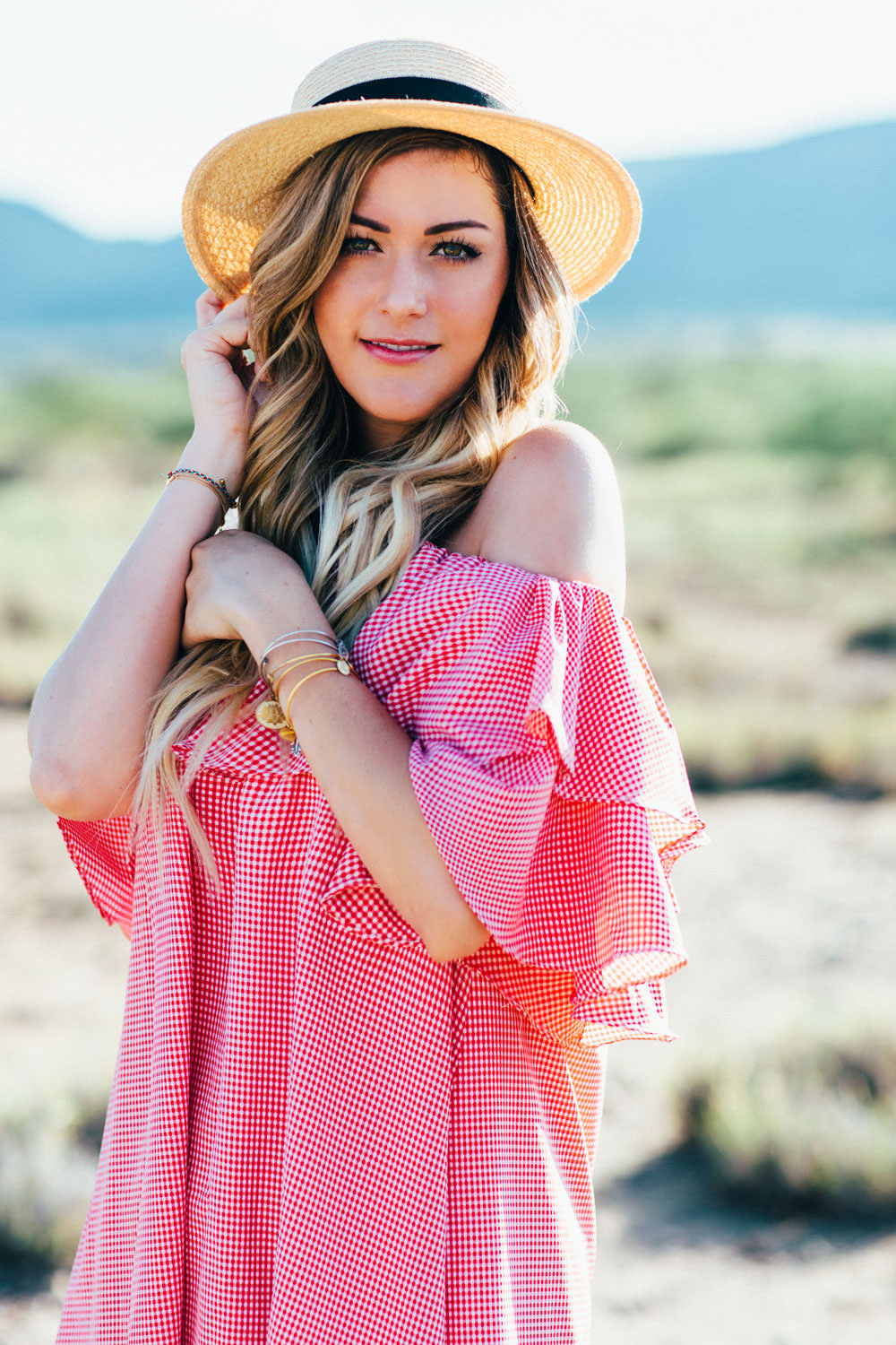 Dash of Darling styles a red gingham off shoulder ruffle dress for summer with a straw bow boater hat by Eugenia Kim and Alex and Ani charm bangles.